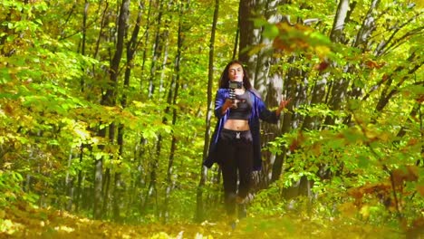 Blogging-charismatic-young-woman-is-walking-in-sunny-autumn-forest-and-recording-video-for-vlog-using-camera-slow-motion