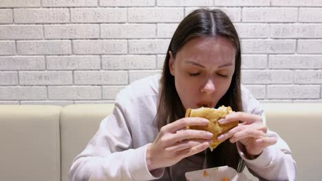 Woman-eating-a-hamburger-with-relish-and-delight-in-cafe.