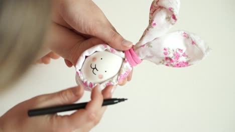 Women's-and-children's-hands-hold-chicken-egg-decorated-for-Easter-bunny-in-hands,-draw-rabbit's-face-with-marker.