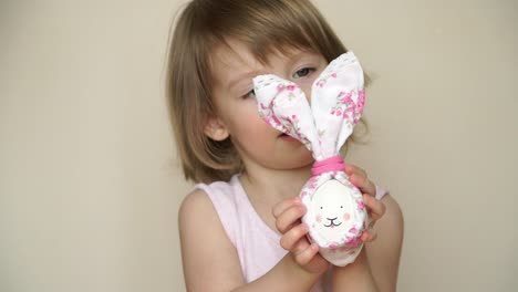 Portrait-of-little-pretty-smiling-caucasian-girl-holds-in-hand-chicken-egg-decorated-for-Easter-bunny,-with-painted-muzzle-and-ears.