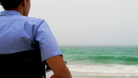 Rear-view-of-African-American-man-sitting-on-wheelchair-at-beach-4k