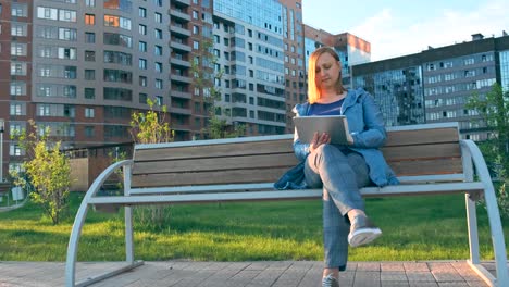 Mujer-usando-tableta-de-ordenador-sentada-en-el-banco-en-la-ciudad