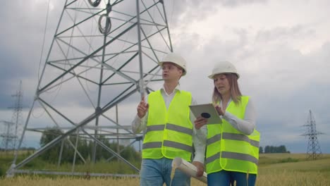 Power-lines,-man-and-woman-engineers-with-a-tablet-in-their-hands-check-the-progress-of-the-installation-of-new-towers-and-analyze-the-network.