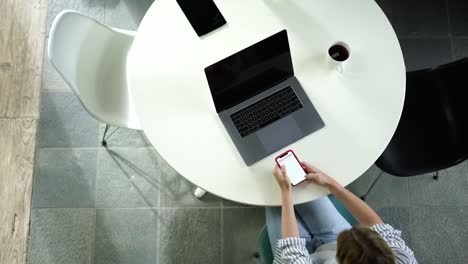 Top-view-of-young-millennial-hipster-girl-using-modern-technologies-for-networking-while-sitting-at-home-interior-table-with-laptop-computer-and-using-smartphone-for-chatting