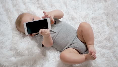 Nettes-Baby-hält-Telefon-in-den-Händen.-Das-Kind-spielt-mit-dem-Handy,-untersucht-es,-zerrt-in-seinen-Händen-und-versucht,-Smartphone-in-den-Mund-zu-nehmen