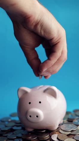 Man-putting-coins-in-piggy-bank-of-pig-shape-in-pile-of-coins,-vertical-video