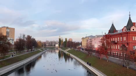 Panoramic-sunset-view-of-the-river,-promenade,-old-churches.-People-from-the-shore-feed-the-ducks