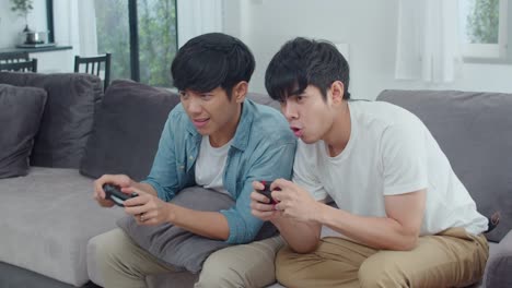 Young-Asian-gay-couple-play-games-at-home,-Teen-korean-LGBTQ-men-using-joystick-having-funny-happy-moment-together-on-sofa-in-living-room-at-house.-Slow-motion-shot.