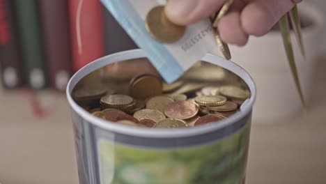 Mano-masculina-toma-un-puñado-de-monedas-de-euros-y-billete-de-banco-de-un-frasco