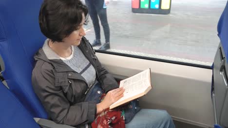 Caucasian-woman-sits-in-train-by-window-Reads-book-Train-stops-on-platform