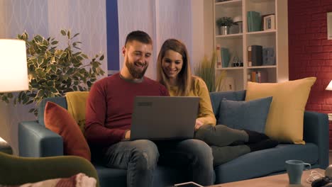 Happy-couple-sitting-on-the-sofa-and-connecting-with-their-laptop