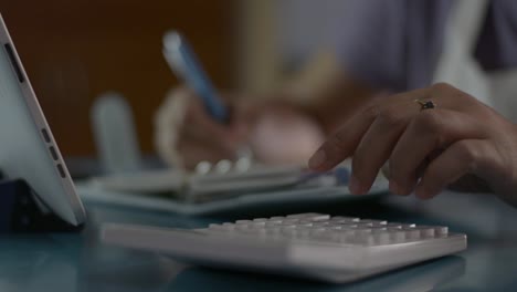 Close-up-hand-of-woman-checking-account-balance-and-calculating-expenses-in-the-living-room-at-home.-Housewife-working-with-calculator-and-take-note-on-the-desk-during-quarantine-with-COVID-19-pandemic-situation.