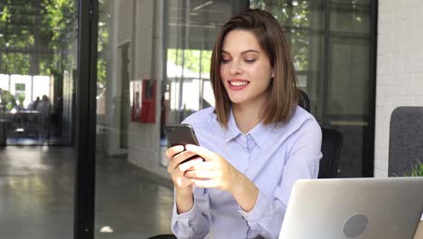 Divertido-y-eufórico-joven-mujer-enviando-mensajes-de-texto-en-el-teléfono-inteligente-en-la-oficina-moderna.-Chica-emocionada-recibir-leer-buenas-noticias-en-el-teléfono-celular.