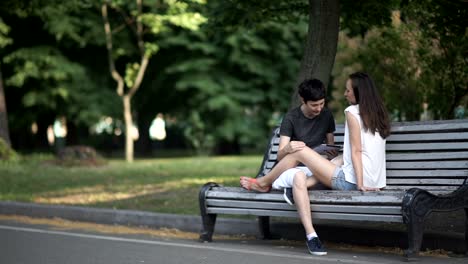 Two-lesbians-use-tablet-and-relax-on-bench-in-park