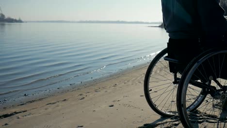 Disabled-man-sits-on-wheelchair-while-on-his-laptop,-nature-on-waterfront-near-river