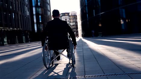 Back-view-of-a-disabled-businessman-in-wheelchair,-moves-in-business-district