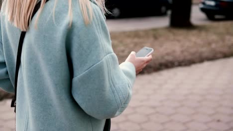 Slow-motion-blonde-teen-in-blue-coat-texting.-Side-view.-Girl-with-long-hair-reading-from-smartphone.-Web-streaming