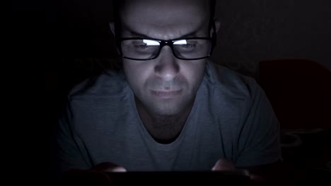 Close-up-of-man-with-glasses-using-smartphone.-Young-man-with-tablet-computer.-A-man-at-night-on-social-networks-using-a-smartphone.