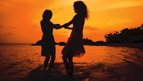 dos-chicas-baila-felices-cogidos-de-la-mano-en-la-playa-al-atardecer-en-cámara-lenta