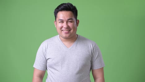 Young-handsome-overweight-Asian-man-against-green-background