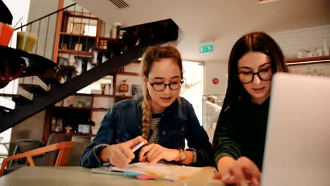 Young-teenage-girls-studying-together-using-laptop-at-urban-café