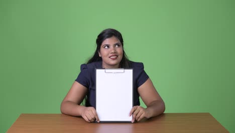 Young-overweight-beautiful-Indian-businesswoman-against-green-background