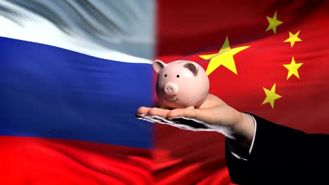 Russland-Investitionen-in-China,-Hand,-Geld-im-Sparschwein-auf-Flagge-Hintergrund