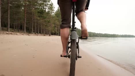 A-barefooted-man-riding-a-bicycle-on-the-beach.-Relaxing-while-having-a-vacation-by-the-lake.