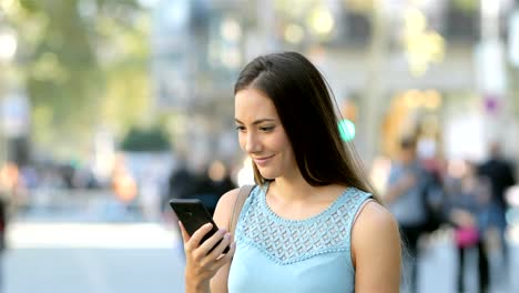 Excited-woman-reading-news-in-a-phone-in-the-street