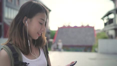 Asian-backpacker-blogger-woman-using-smartphone-for-chat,-check-social-media-and-listen-to-music-while-traveling-at-Chinatown-in-Beijing,-China.-Lifestyle-backpack-tourist-travel-holiday-concept.