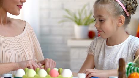 Hija-elegir-huevo-rosa-en-manos-de-las-madres,-familia-jugando-en-los-juegos-de-Pascua