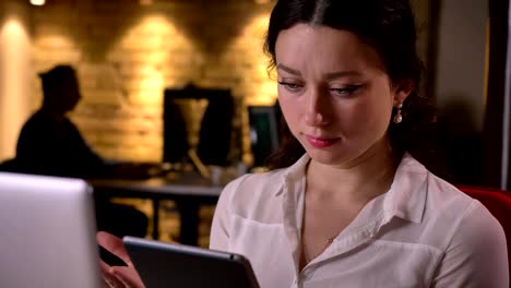 Closeup-of-young-caucasian-female-office-worker-scrolling-on-the-tablet-and-being-confused-indoors-on-the-workplace