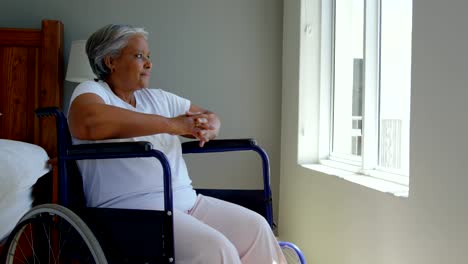 Seitenansicht-der-Behinderung-senior-schwarze-Frau-sitzen-im-Rollstuhl-in-der-Nähe-von-Fenster-im-Schlafzimmer-zu-Hause-4k