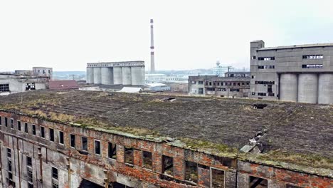 Ein-alter-verlassener-Fabrikhangar-mit-beschädigten-Wänden-auf-dem-Hintergrund-anderer-alter-Bauwerke-im-gleichen-Bereich.