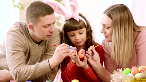 Das-Mädchen-hält-ein-Osterei,-und-Papa-und-Mama-schmücken-es.