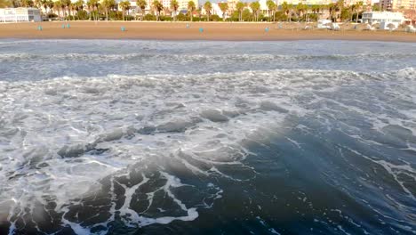 Olas-del-mar-Mediterráneo-llegan-a-la-orilla,-la-cámara-sube-lentamente-y-muestra-la-ciudad-de-Valencia