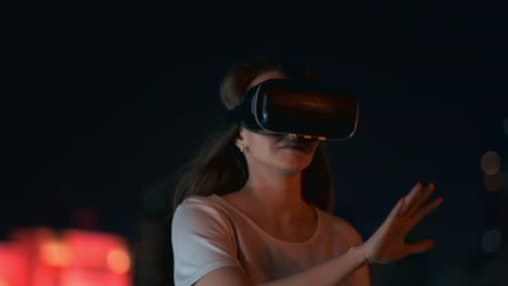 Junge-Frau-in-Virtual-Reality-Brille-in-der-Nachtstadt-bewegt-ihre-Hände