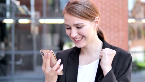 Outdoor-Young-Businesswoman-Excited-for-Success-on-Smartphone