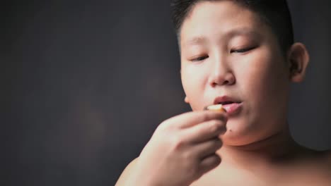 large-build-Asian-preteen-boy-eating-donut-while-touching-his-tummy,-slow-motion-in-low-light.