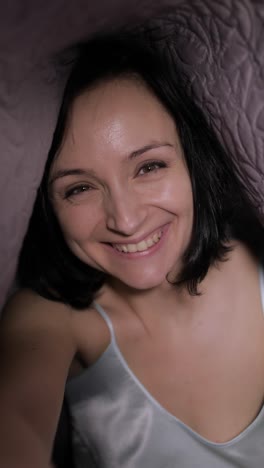 Woman-sitting-on-bed-under-blanket.-Enjoying-video-chat-to-friend-on-smartphone