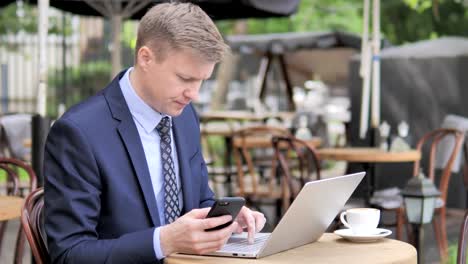 Geschäftsmann-nutzt-Smartphone-und-Laptop-im-Outdoor-Cafe