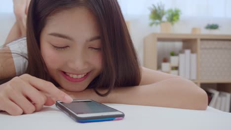 Slow-motion---Young-Asian-woman-using-smartphone-checking-social-media-feeling-happy-smiling-while-lying-on-bed-after-wake-up-in-the-morning,-Attractive-Japanese-girl-smiling-relax-in-bedroom-at-home.