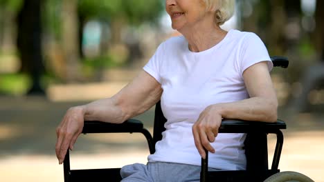 Mature-woman-sitting-in-wheelchair-on-hospital-territory,-rehabilitation