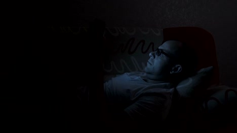 Close-up-of-man-with-glasses-using-smartphone.-Young-man-with-tablet-computer.-A-man-at-night-on-social-networks-using-a-smartphone.-Man-with-tablet-computer-lying-on-sofa