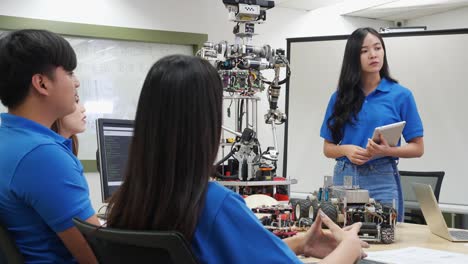 La-mujer-ingeniera-asiática-presenta-la-innovación-de-robots-con-el-equipo-de-diseño-de-arquitectos-en-laboratorio.-La-reunión-en-equipo-comparte-ideas-tecnológicas-y-un-robot-de-desarrollo-colaborador.-Concepto-de-tecnología-robótica-de-presentaci�