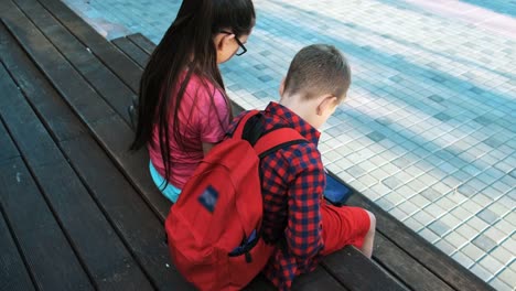 The-older-sister-and-brother-are-sitting-on-the-street,-looking-at-smartphones.