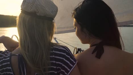 lesbian-couple-hugging-on-sailboat-floating-on-river-at-sunset