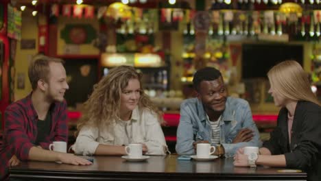 Happy-multiracial-young-people-friends-talking-laughing-at-group-meeting-sharing-cafe-table,-diverse-students-drinking-coffee-having-fun-together-enjoy-multi-ethnic-friendship-pleasant-conversation.