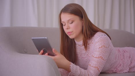 Closeup-portrait-of-young-attractive-caucasian-female-using-tablet-being-surprised-laying-on-couch-indoors-in-apartment