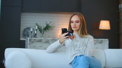 Una-mujer-feliz-y-sonriente-tiene-un-teléfono-inteligente-en-sus-manos-y-hace-compras-en-línea-utilizando-un-banco-móvil.